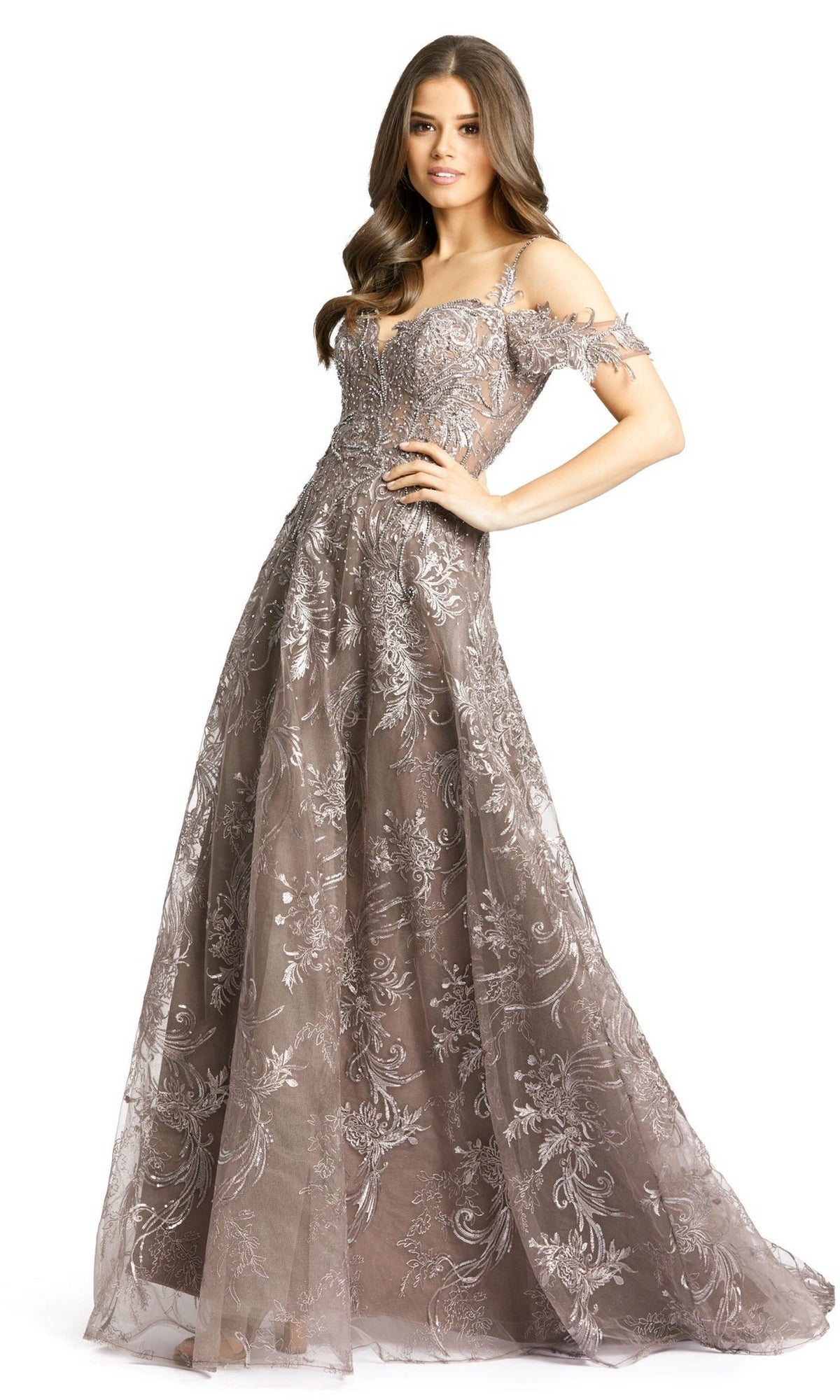 A woman poses against a white background in the Long Formal Dress 20287 by Mac Duggal, a floor-length A-line silver lace dress with floral embroidery and a subtle sweetheart neckline.